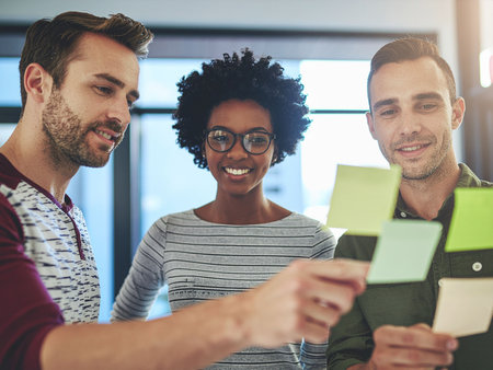 Portrait of smiling business people working together in office. They are holding sticky notes and looking at cameraの素材