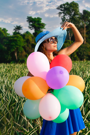 Young beautiful girl in a blue hat with colorful balloons in vintage glassesの写真素材