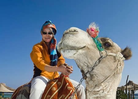 Two smiles. On a white camel sits a smiling woman in a yellow jacket and a bright turban. The camel turned its head in the direction of the rider and also smiles.の写真素材