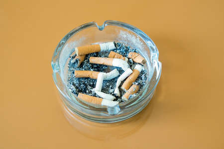 cigarettes in glass ashtray isolated on brown backgroundの写真素材