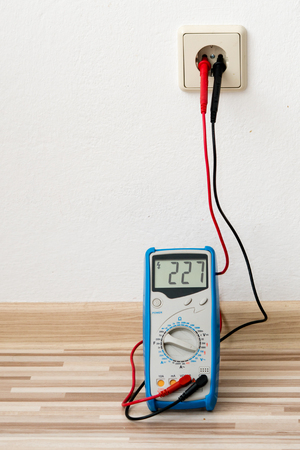 Voltage measuring with digital multimeter instrument on wall socket in home room.の写真素材