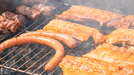 Assortment of marinated meat grilling over the hot coals on a BBQ with sausage, steak. Closeup.