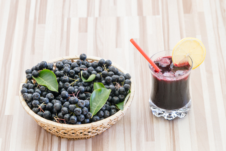 Fresh juice of chokeberry (Aronia melanocarpa) in glass and berry in pot on wooden backgroundの写真素材