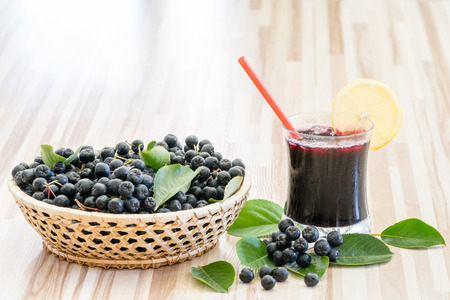 Fresh juice of chokeberry or Aronia melanocarpa in glass and berry in pot on wooden backgroundの写真素材
