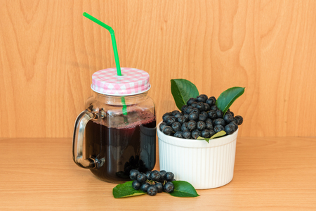 Chokeberry or Aronia melanocarpa juice with ice in glass with straw and berry in basket near on wooden backgroundの写真素材