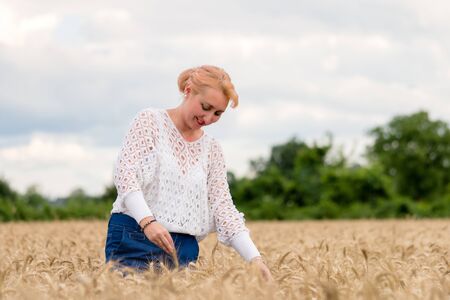 Beautiful woman stand in golden wheat field and hold ear of wheat, with cloudy blue sky background, free space. Liberty, peace of mind, happy summer or agriculture concept.の写真素材