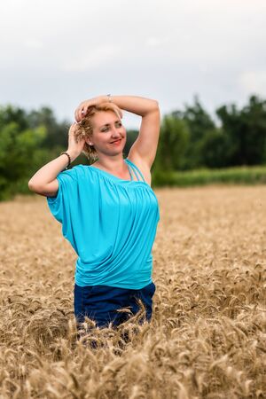 Beautiful romantic woman in white shirt and jeans stand in the golden wheat field. Happy summer or agriculture concept.の写真素材