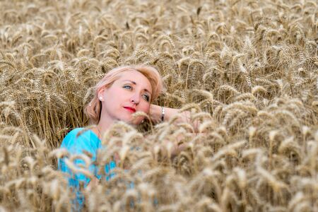 Portrait of beautiful woman with green eyes sitting in golden wheat field and look in the sky. Liberty, love, happy summer, peace of mind or relaxation concept.の写真素材