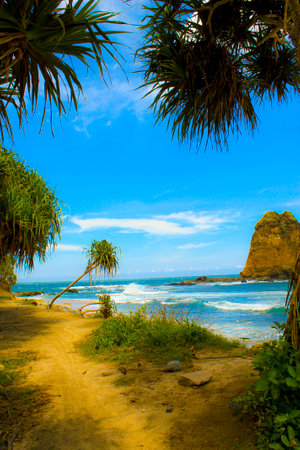 An Indonesian beach with beautiful tropical views, has rocks in the middle of the sea, lush leaves and trees and clear sea waterの写真素材