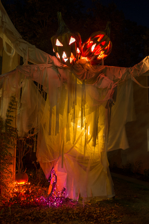 A scary display of a two headed pumpkin ghost at night with yellow up lighting that adds to this halloween looking displayの写真素材