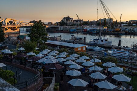 Victoria, Vancouver Island, British Columbia, Canada, July, 8, 2019; looking across the umbrellas outside the Canoe Brew Pub in Victoria at sunset, the golden light reflecting off the bridgeのeditorial素材