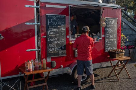 Victoria, Vancouver Island, British Columbia, Canada, July, 8, 2019: A man in a red shirt ordering from a re food stall the famous and traditional  Canadian dish poutineのeditorial素材
