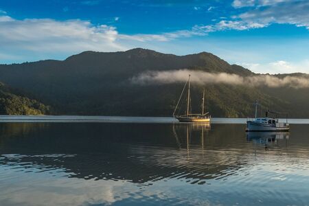 Two boats sitting on flat calm waters of the the Marlborough Sound, reflection of the boats in the...