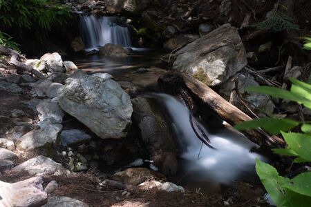 A small multi-tiered waterfall with rocks and green foliage, long exposure shot to smooth out the cascading waterの写真素材
