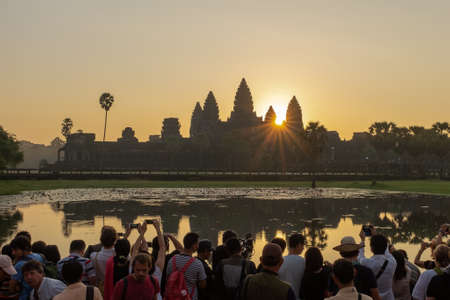 Angkor Wat, Siem Reap, Cambodia, November, 4, 2014: A large crowd of photographers crowd round the edge of a lake facing Angkor Wat to grab the perfect sunrise shot, their reflection in the lake waterのeditorial素材
