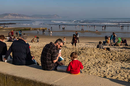 A father and son enjoying the unseasonable warm weather on Lyme Regis sea front, the beach is crowded with people, a typical English sea side imageのeditorial素材