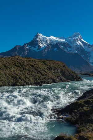 Waterfall cascading with a thunderous roar with a mountain range in the background, Torres del Paine, National Park, Chile, clear blue sky, portrait aspectの写真素材
