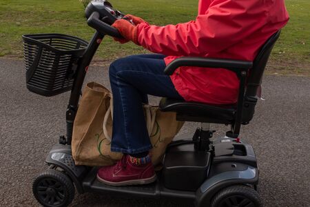 A side on shot of an elderly lady in a red coat enjoying the freedom of an electric mobility scooter, from the shoulders downの写真素材