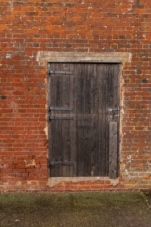 A close up of a wooden seasoned barn door in a brick wall of a out building on a farmの写真素材