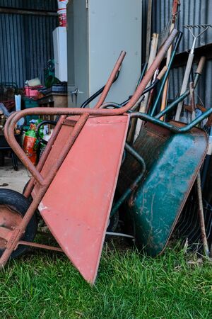 Pink and green wheel barrows and garden tools stacked in an open barnの写真素材