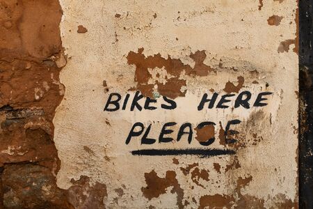 A close up of a hand painted sign on where to leave your bike on an exposure brick wall with the plaster falling awayの写真素材