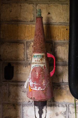 A vintage red fire extinguisher hanging on a wall with a  faded label and cone shapedの写真素材