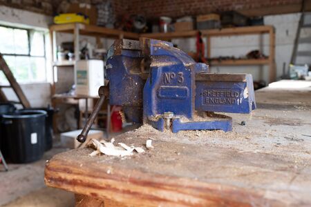 A close up of a blue vice on a wooden worktop in a workshop covered in wood cutting dustの写真素材