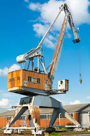 An old, orange colored, discarded dockside crane at a sunny day with blue sky