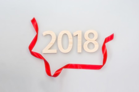 Wooden figures forming 2018, carved from light wood on a gray background with a red ribbon. New Year Idea, postcard, poster, greetings. Festive decor.の写真素材