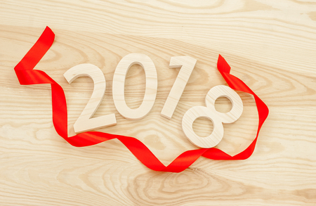 New Year's concept. Figures 2018 carved from wood on the background of a polished board framing a red ribbonの写真素材