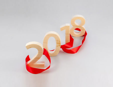 Wooden figures forming 2018, carved from light wood on a gray background with a red ribbon. New Year...