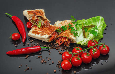 Shawarma cut with chicken meat on black background close-up. Cheese, red pepper parsley. Street Food, Fast Food, Oriental Food.の写真素材