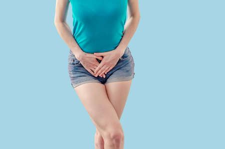 Young woman in shorts and a T-shirt is experiencing pain in the womb, pressed her hands to the lower...