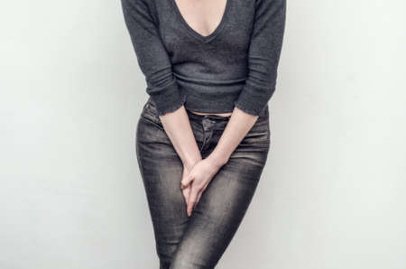 Young slim girl in jeans holds hands pressed between her legs. Women's health, gynecology