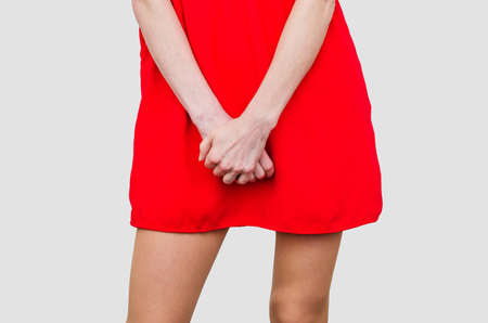 Woman in a red dress holding hands between legs. Experiencing pain, discomfort. Women's health, gynecology.の写真素材