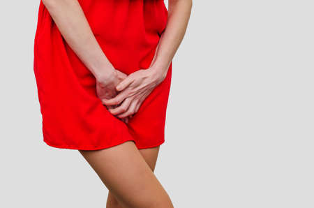 Woman in a red dress holding hands between legs. Experiencing pain, discomfort. Women's health, gynecology.の写真素材