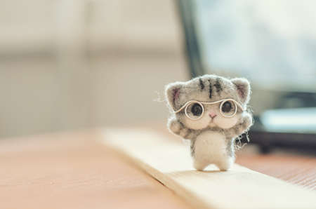 Felting toy little gray kitten in glasses on wooden standの写真素材