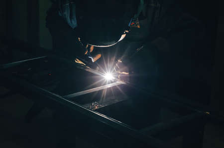 Welding a metal product in metal workshop. Bright glow of an electric arc. Fabrication of metal...