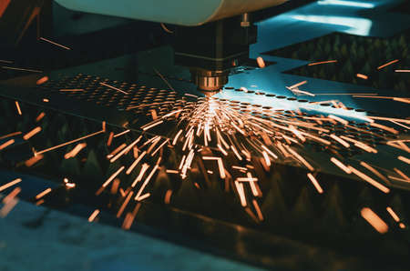 Machine for laser cutting of metal. Laser head cuts the sheet with a beam, sparks scatter in...