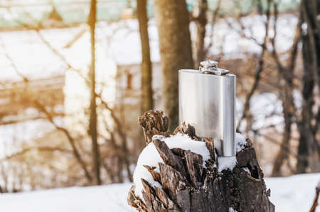 A shiny metal flask for alcohol stands on a tree stump in snow. Nature, winter, rest.の写真素材