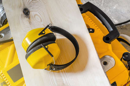 Sound-proof headphones lie on a board on a yellow woodworking machine