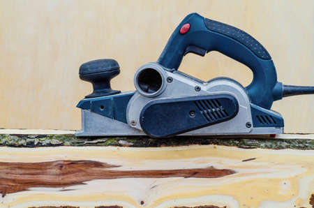 Manual electric plane on raw tree log. Woodwork. Manufacture of wood products. Carpentry workshopの写真素材