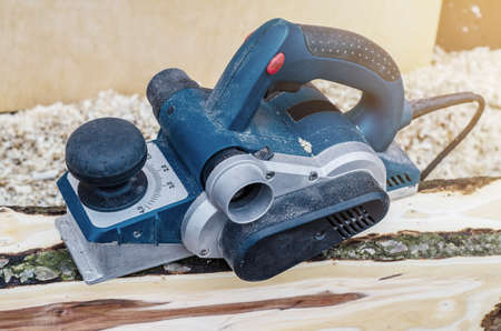 Manual electric plane on raw tree log. Woodwork. Manufacture of wood products. Carpentry workshopの写真素材