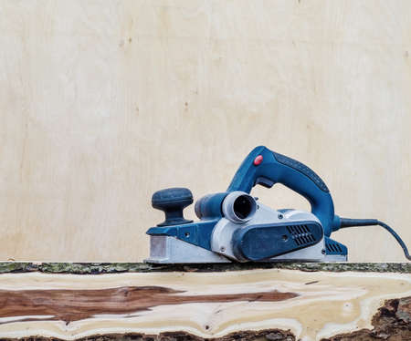 Manual electric plane on raw tree log. Woodwork. Manufacture of wood products. Carpentry workshopの写真素材