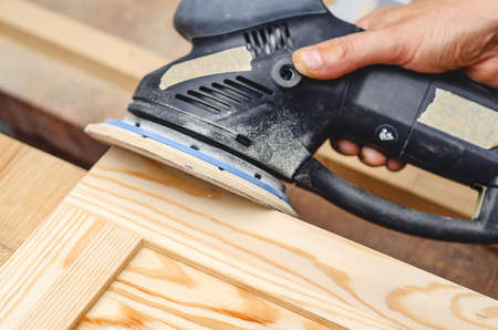 Sanding a wooden board with ahand-held electric sander