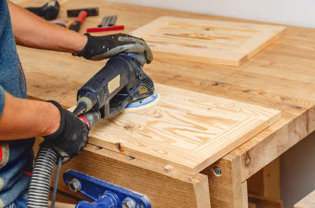 Sanding a wooden board with a hand-held electric sander