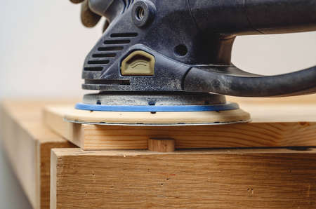 Joiner's tools. Sanding a wooden board with a hand-held electric sander