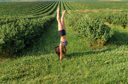 Woman with black hair doing exercises in the field. She is standing on her hands. Short black shorts...