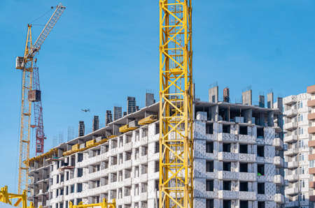 Construction of multi-storey building.Yellow and blue cranes. Sunlight on construction site.