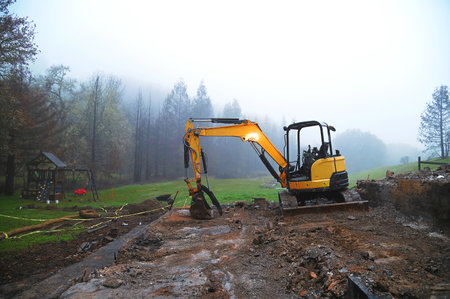 Yellow small excavator clears the area after a fire in the fog in the evening
